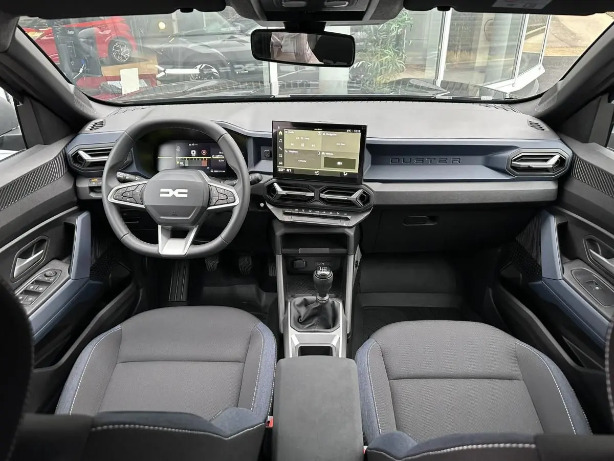 Vue intérieure frontale du tableau de bord noir du Dacia Duster 2025 avec écran tactile et boîte manuelle.