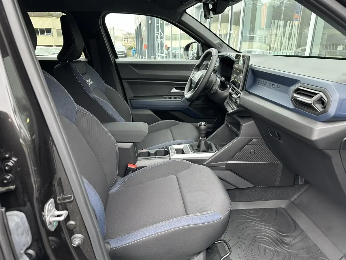 Vue intérieure côté conducteur du Dacia Duster noir 2025, montrant sièges tissu bicolore et tableau de bord moderne.