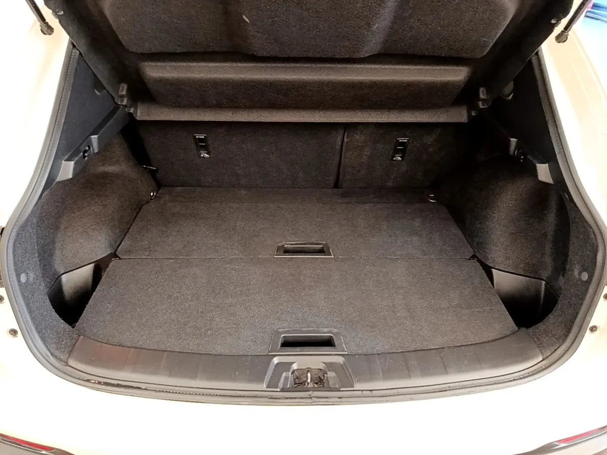 Coffre ouvert vu de face d’un Nissan Qashqai blanc, montrant l’espace de chargement avec banquette rabattue.