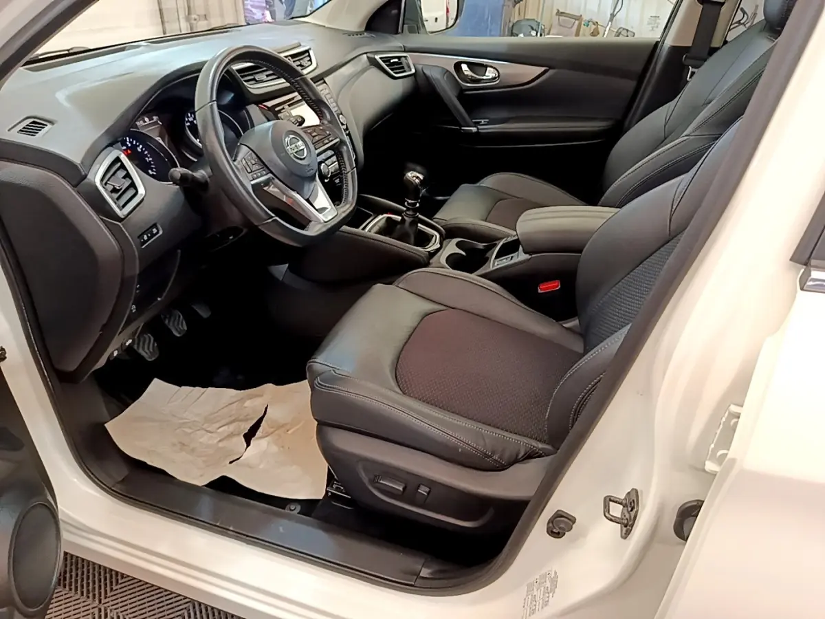 Vue intérieure côté conducteur du Nissan Qashqai blanc 2019, avec sièges cuir noirs et volant multifonctions.