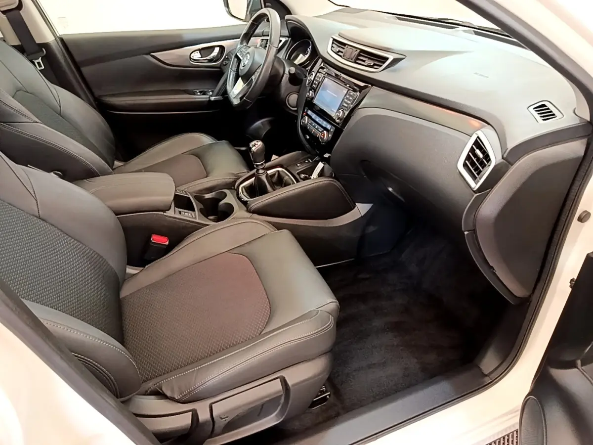 Intérieur avant droit du Nissan Qashqai blanc 2019, sièges noirs, tableau de bord avec écran tactile et boîte manuelle.