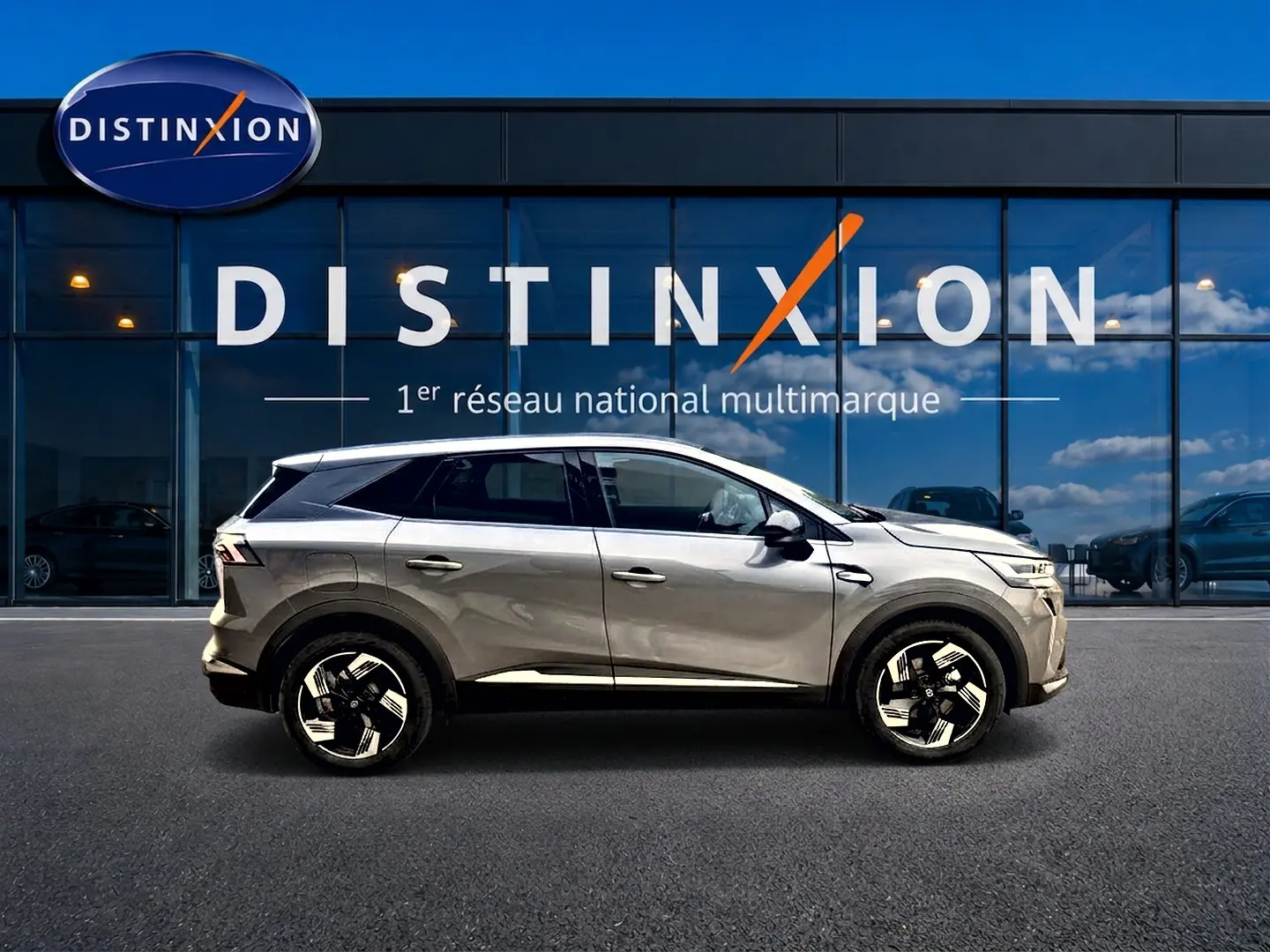 Profil côté gauche du Renault Symbioz gris cassiopée 2026, avec jantes alu et vitres surteintées devant une vitrine Distinxion.