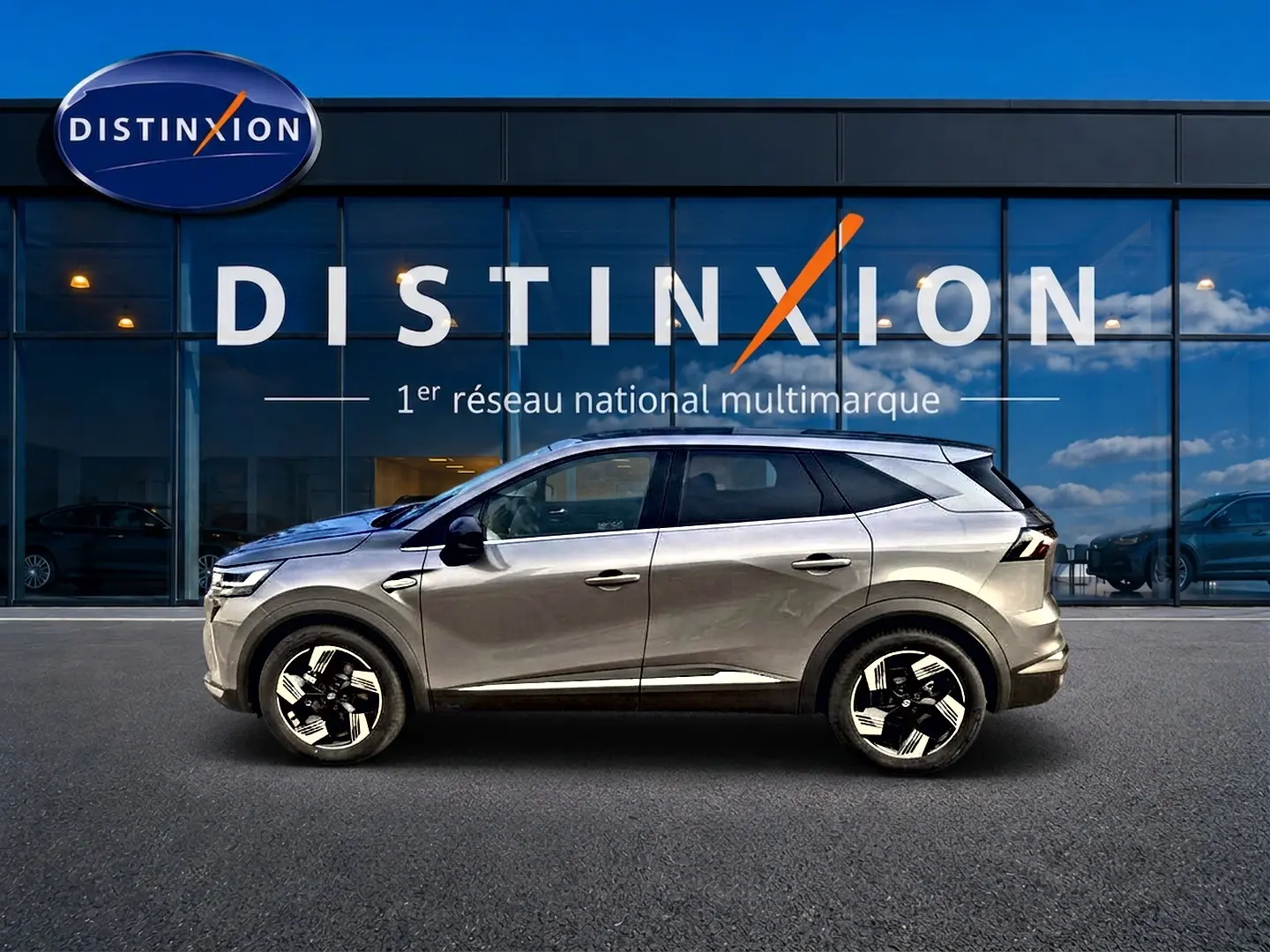 Profil droit du Renault Symbioz gris cassiopée 2026, SUV hybride avec jantes alu et vitres surteintées, devant une vitrine Distinxion.