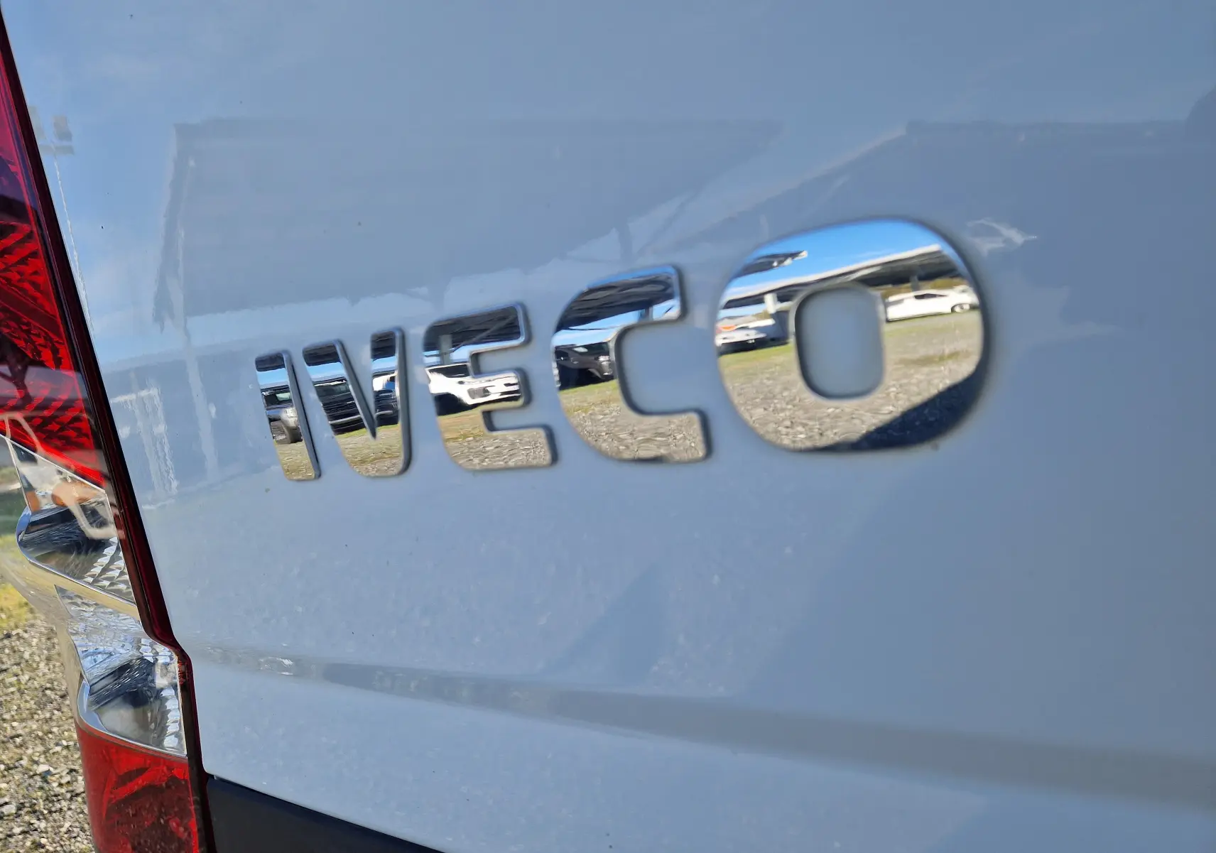 Gros plan sur l'arrière blanc d'un Iveco Daily Fourgon avec logo chromé reflétant l'environnement alentour.