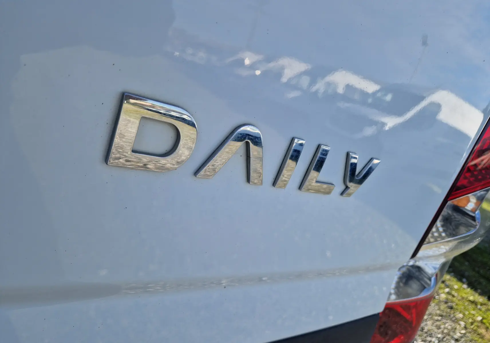 Gros plan sur l'arrière droit blanc d'un Iveco Daily Fourgon 2022 avec logo chromé et feu arrière visible.