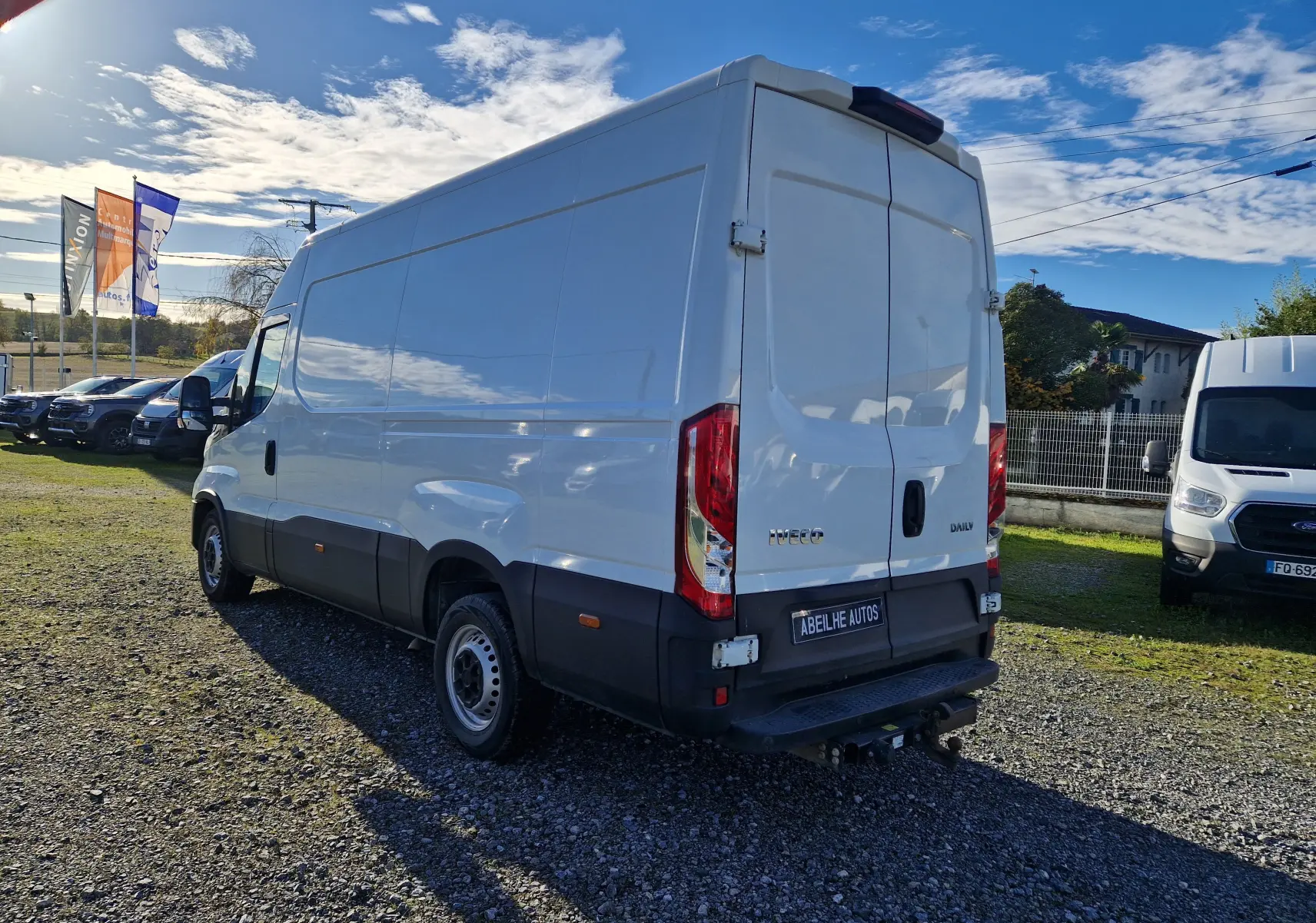 Fourgon Iveco Daily blanc vu en 3/4 arrière droit, avec marchepied arrière et attelage visible, stationné en extérieur.