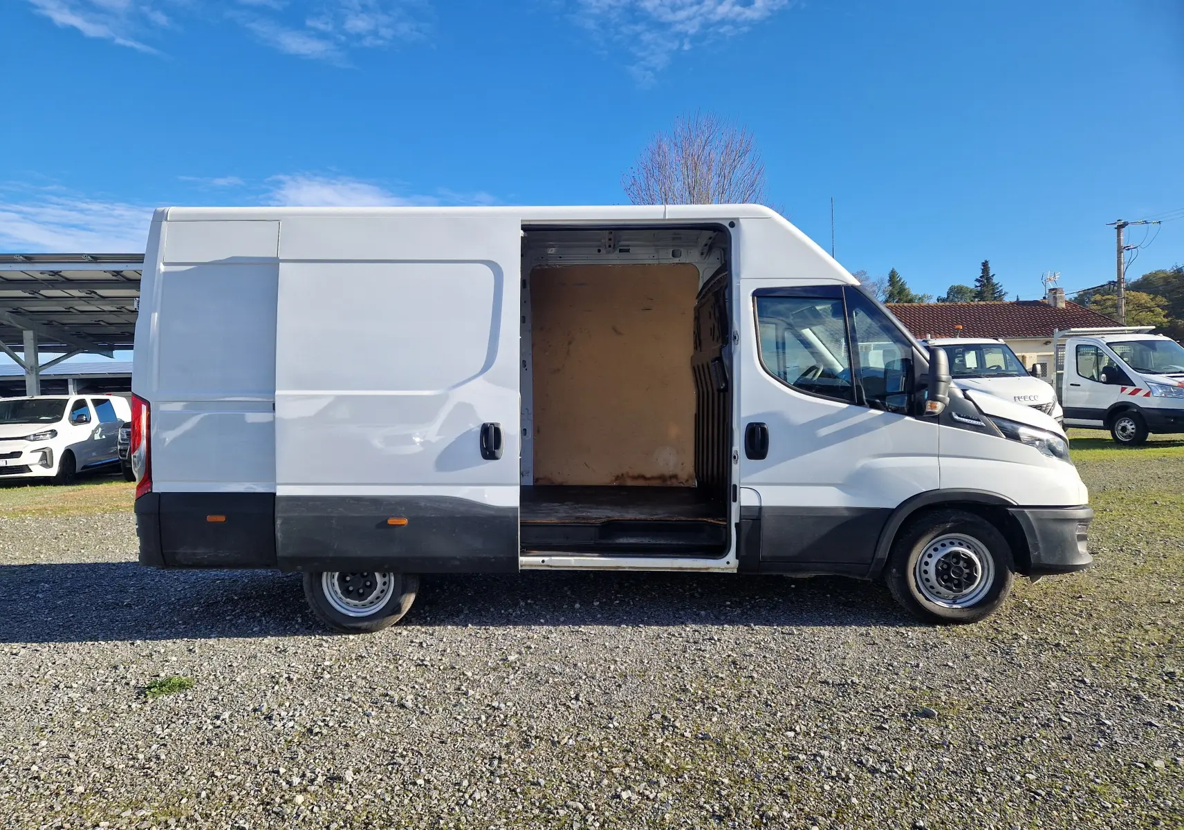 Vue de profil droit d'un fourgon Iveco Daily blanc 2022 avec porte latérale coulissante ouverte dévoilant l'intérieur vide.