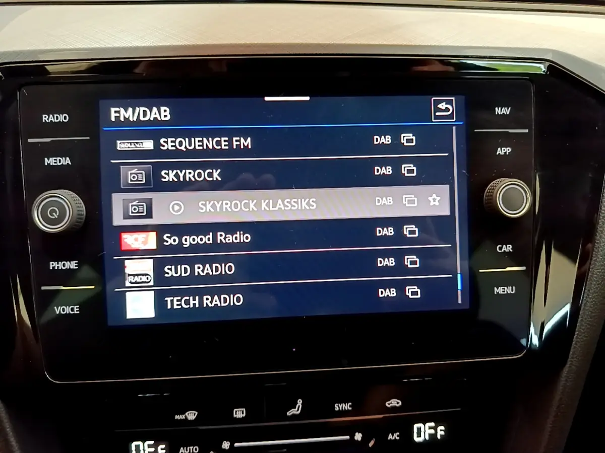 Écran tactile central affichant les stations radio numériques dans l'habitacle d'une Volkswagen Passat gris foncé.