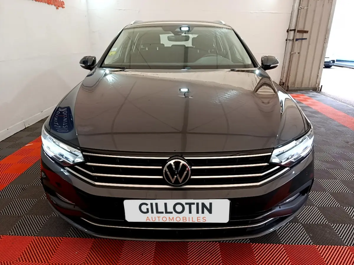 Vue frontale d'une Volkswagen Passat gris foncé 2021 avec calandre chromée et phares LED allumés dans un showroom.