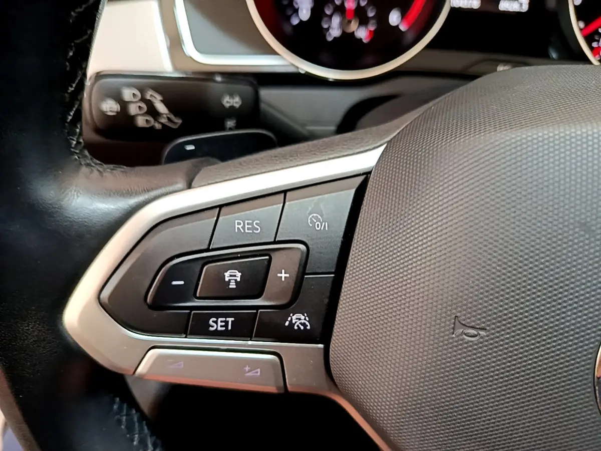 Gros plan sur le volant cuir de la Volkswagen Passat gris foncé, avec commandes de régulateur de vitesse et tableau de bord en arrière-plan.