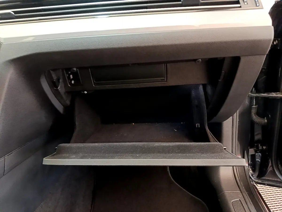 Gros plan sur la boîte à gants ouverte côté passager d'une Volkswagen Passat gris foncé, intérieur noir.