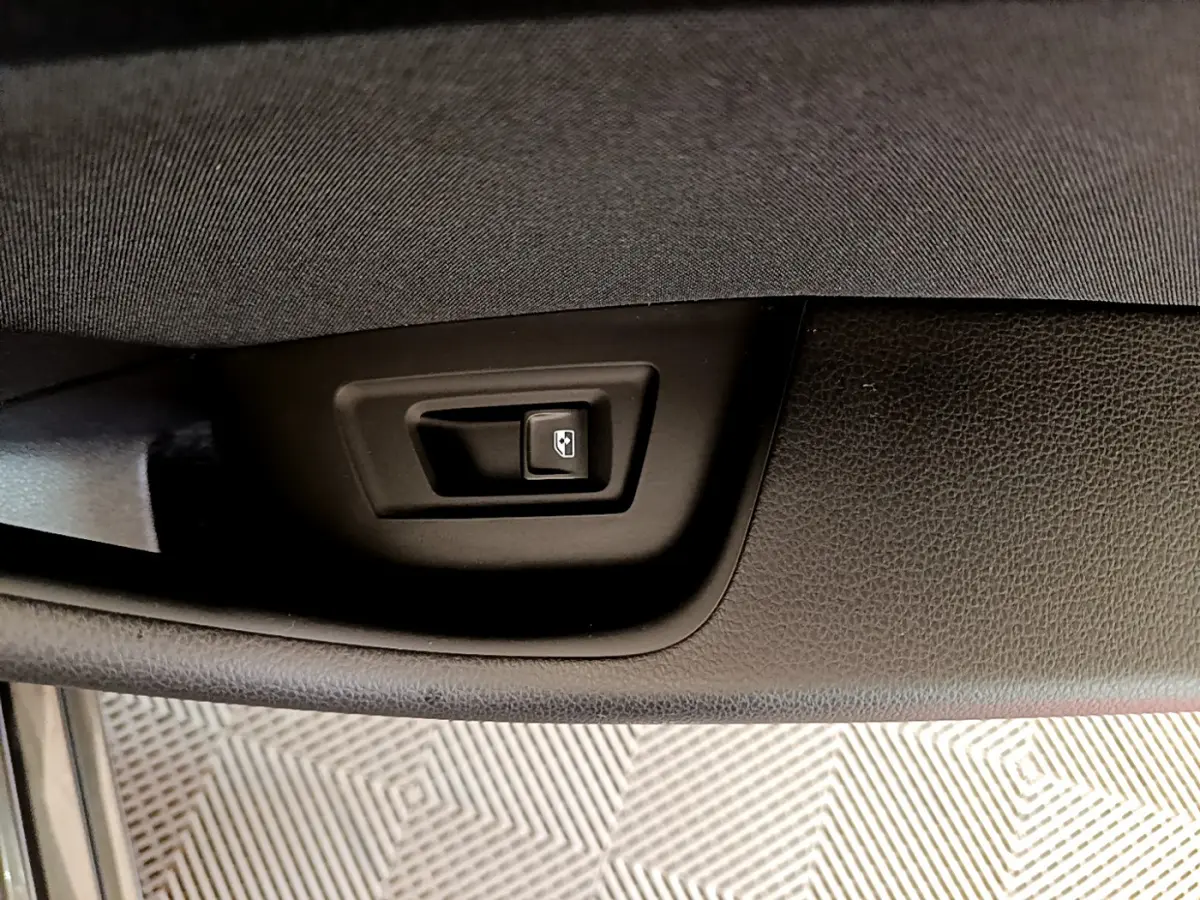 Gros plan sur le bouton d'ouverture du coffre intégré dans le panneau de porte noir d'une Volkswagen Passat gris foncé.