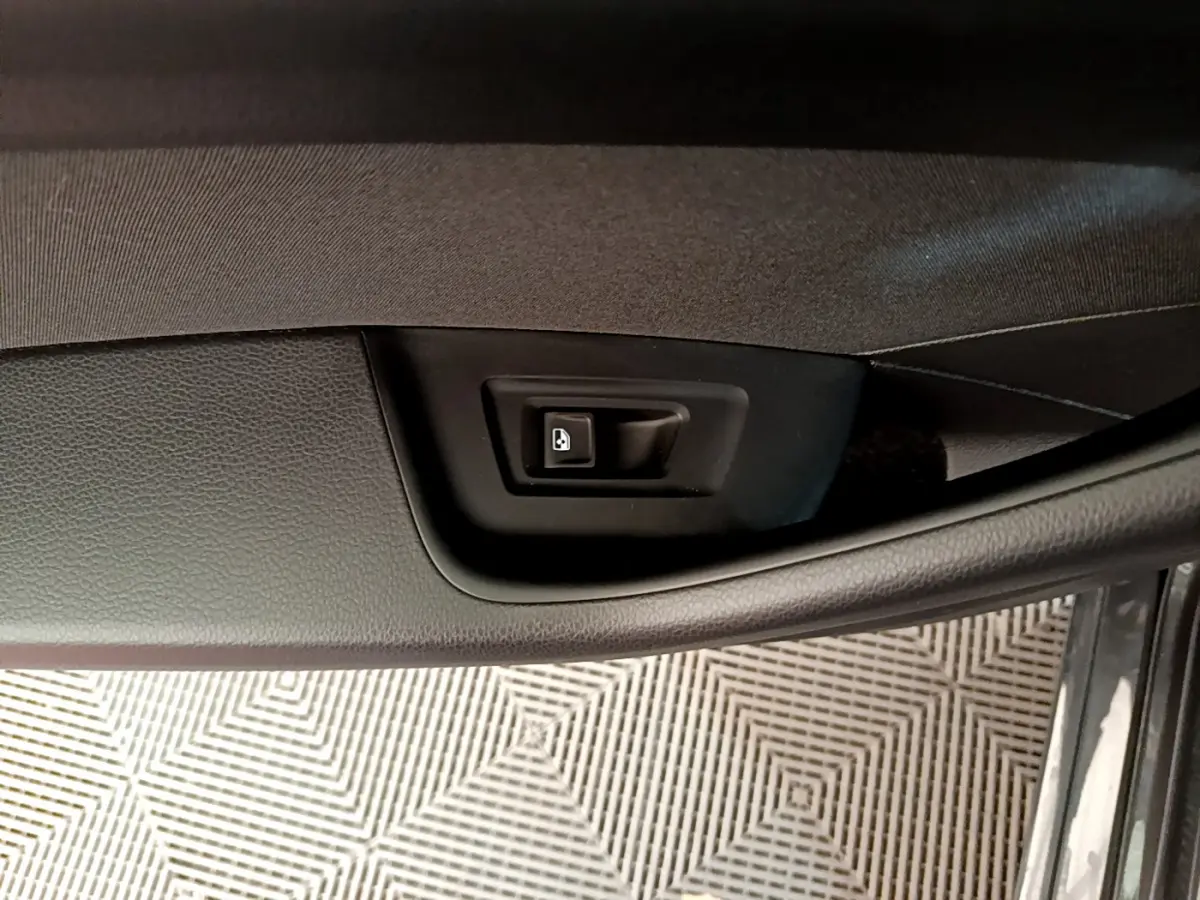 Bouton de déverrouillage électrique de la porte intérieure, sur panneau noir texturé côté conducteur d'une Volkswagen Passat gris foncé.