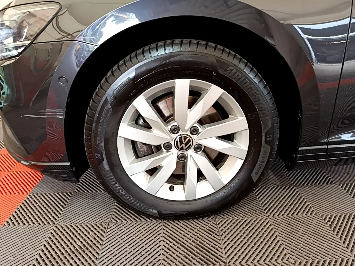 Gros plan sur la roue avant gauche d'une Volkswagen Passat gris foncé, jante alliage et pneu Bridgestone visibles.
