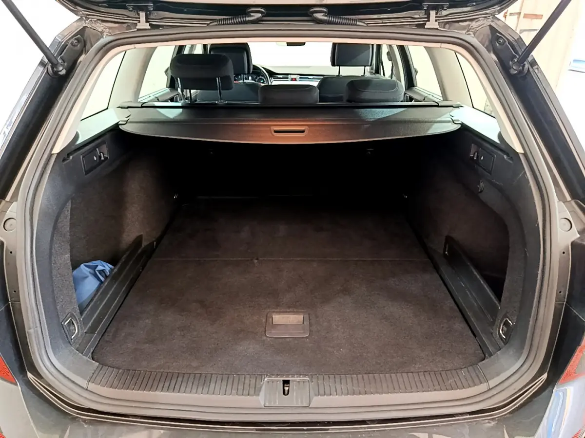 Coffre ouvert d'une Volkswagen Passat gris foncé, vue arrière, montrant l'espace de chargement avec tablette de séparation.