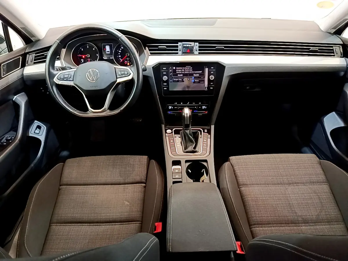 Intérieur avant de la Volkswagen Passat 2021, vue du tableau de bord avec volant cuir et sièges tissu marron.