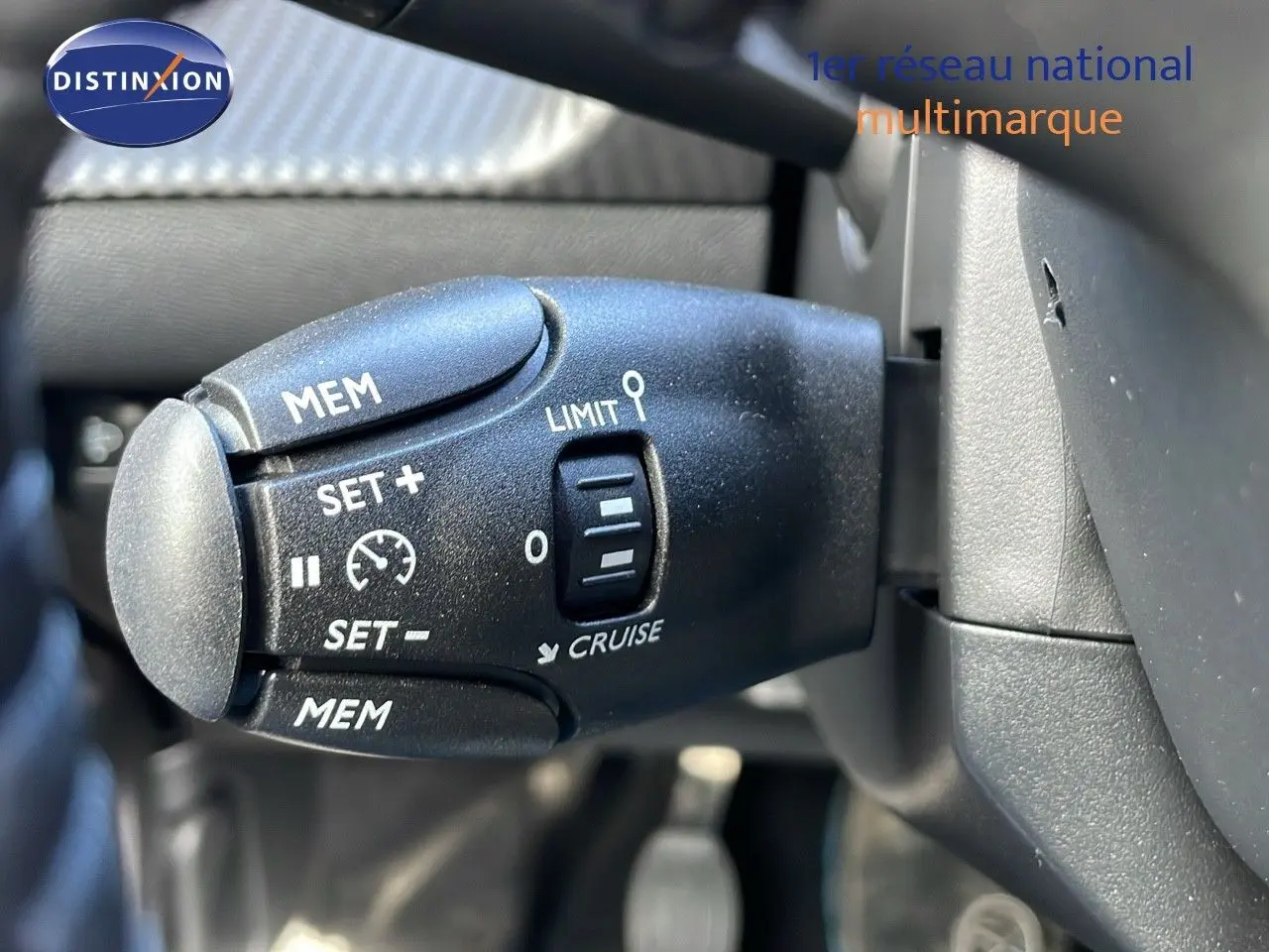 Gros plan sur la commande de régulateur de vitesse à gauche du volant d'un Peugeot 2008 blanc Okenite Metal 2025.