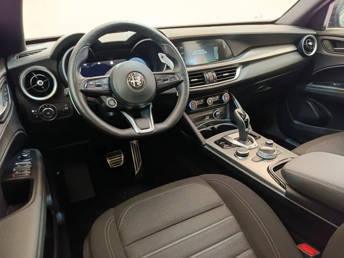 Intérieur noir de l'Alfa Romeo Stelvio 2024, vue côté conducteur sur le volant, tableau de bord et console centrale.