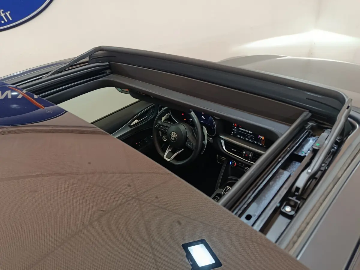 Vue plongeante sur l’intérieur noir d’un Alfa Romeo Stelvio gris foncé 2024 avec tableau de bord digital et toit ouvrant.