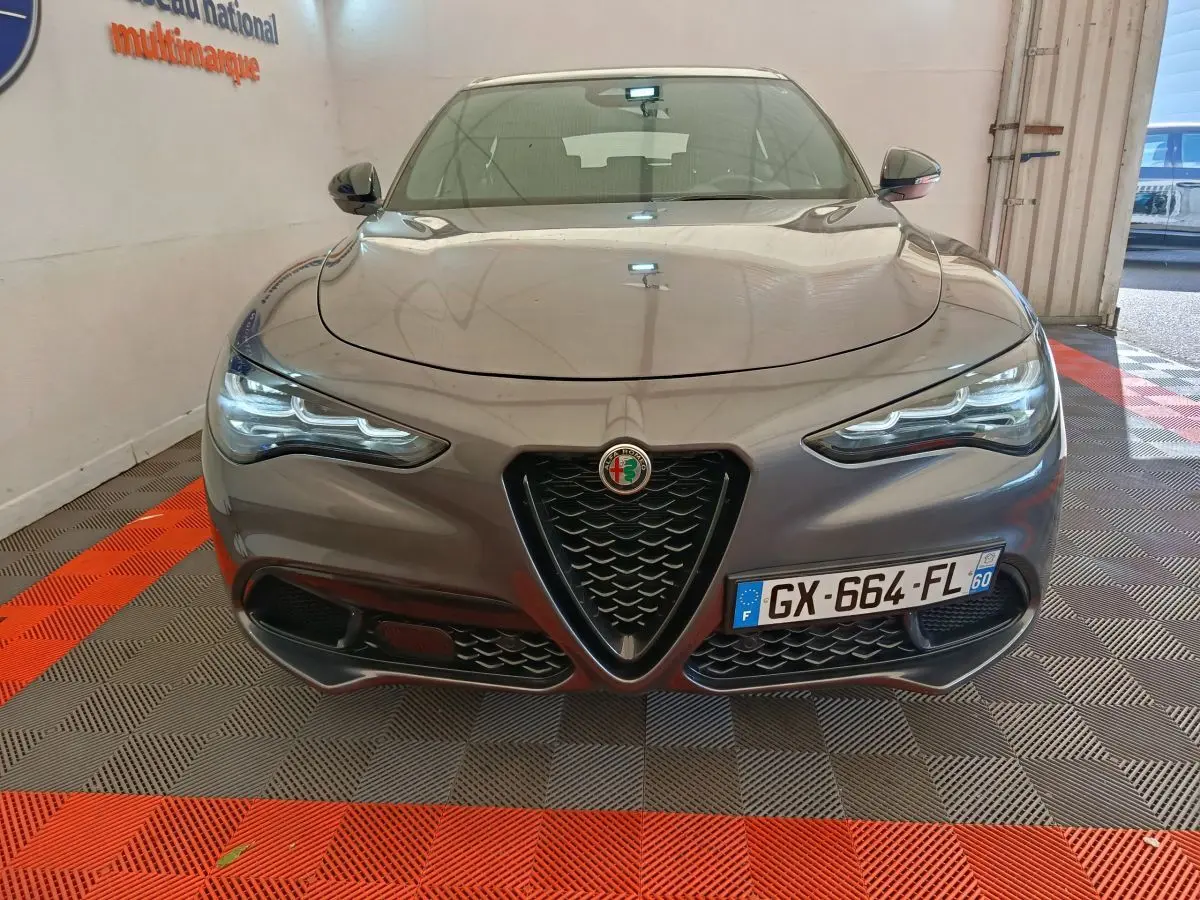 Vue frontale d'un Alfa Romeo Stelvio gris foncé 2024 avec calandre caractéristique en V et phares LED allumés.