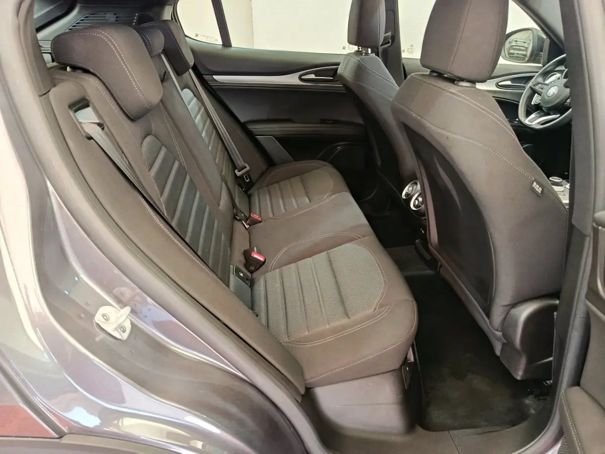Vue côté gauche de l'habitacle arrière gris foncé de l'Alfa Romeo Stelvio 2024 avec sièges en tissu et aérateurs centraux.