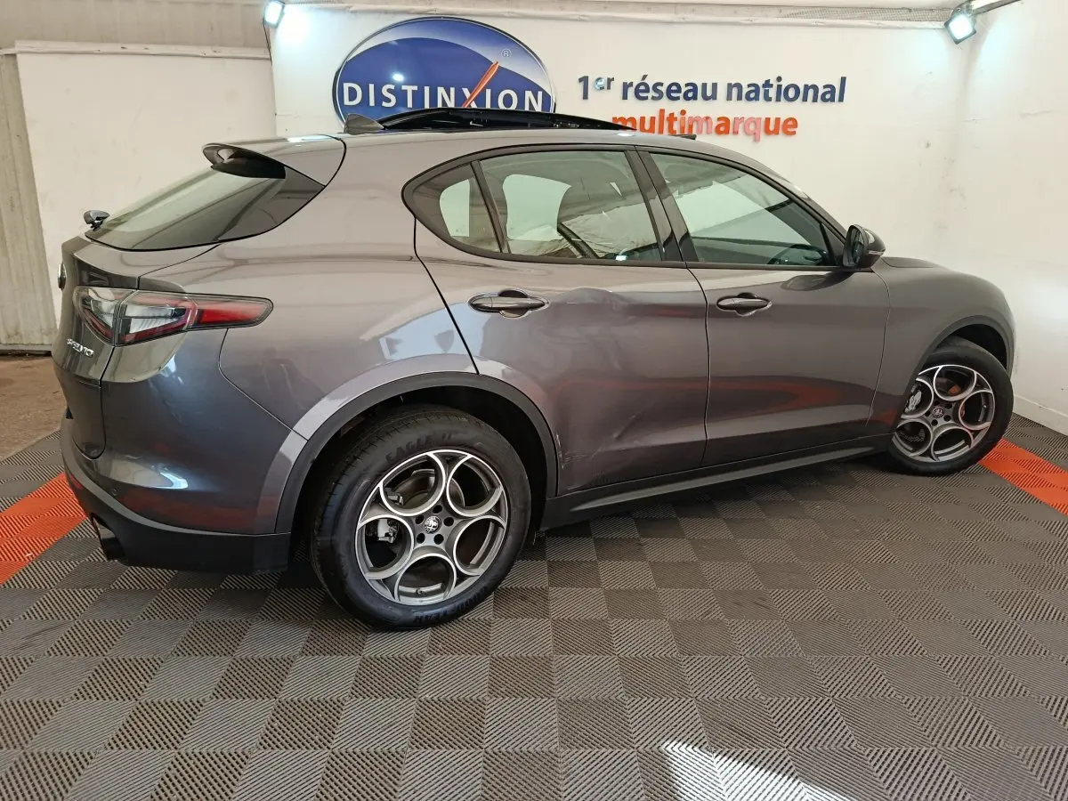 Vue côté gauche d'un Alfa Romeo Stelvio gris foncé 2024 avec jantes sport et feux arrière LED dans un showroom.