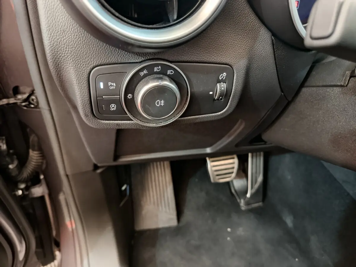 Gros plan sur les commandes d'éclairage et les pédales côté conducteur de l'Alfa Romeo Stelvio gris foncé 2024.