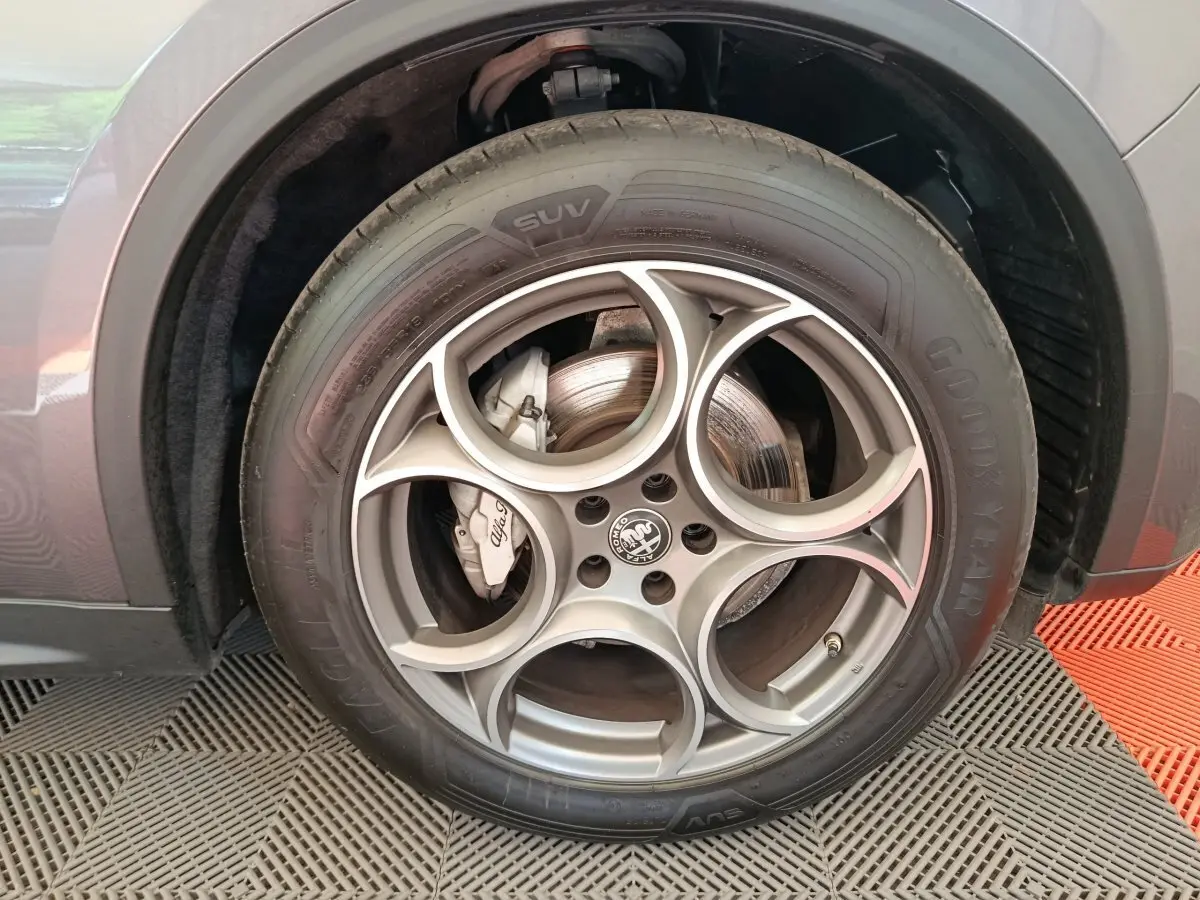 Gros plan sur la roue avant gauche gris foncé de l'Alfa Romeo Stelvio 2.2 TD 160 AT8 Sprint avec jante distinctive à cinq cercles.