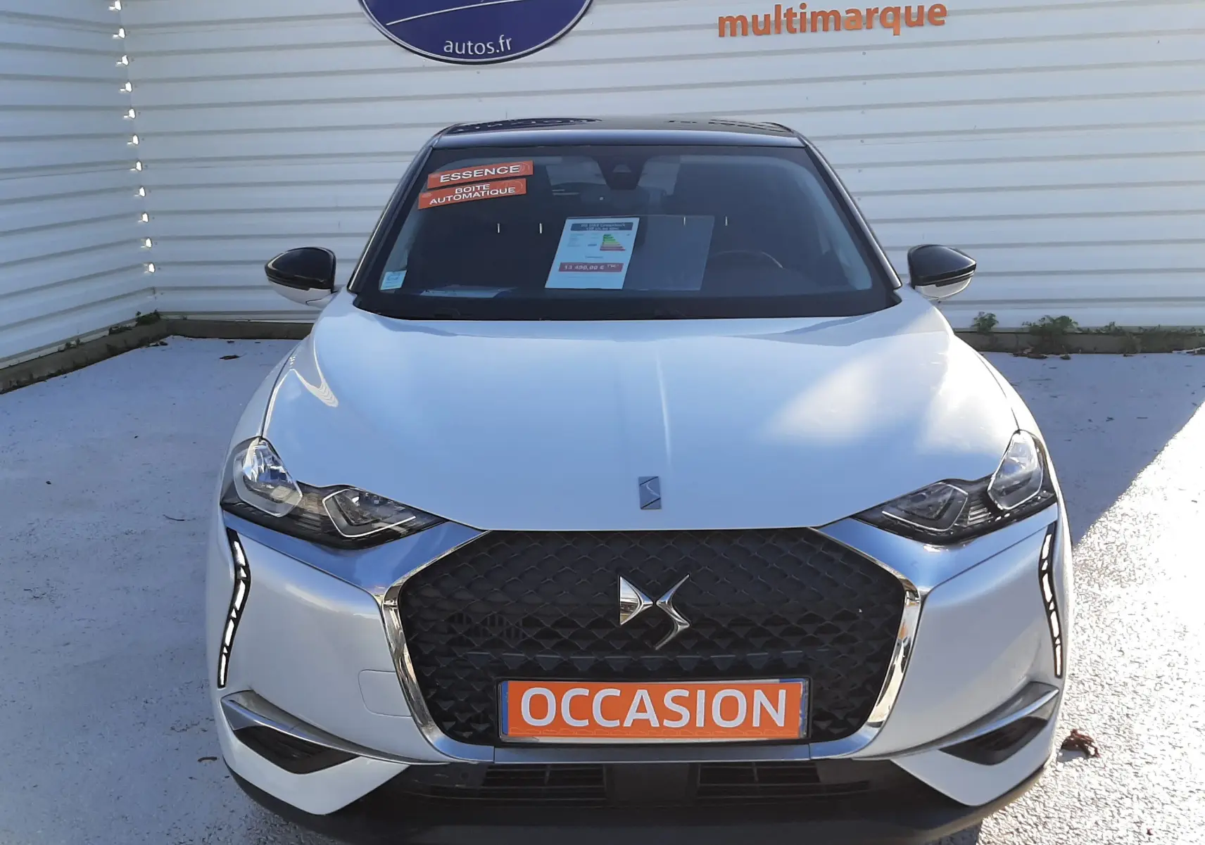 Vue frontale d'un DS3 Crossback blanc perle avec toit noir, calandre noire et plaque orange "OCCASION" visible.