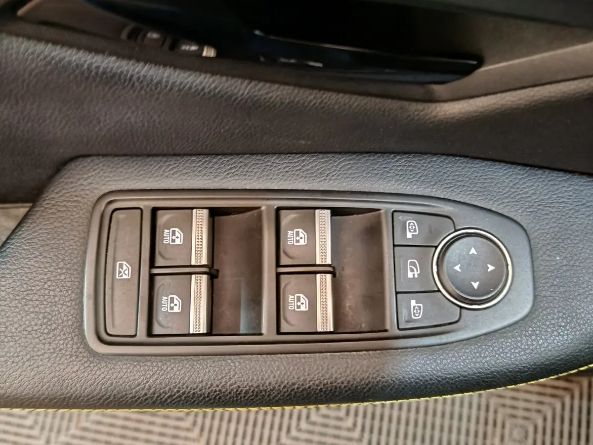 Gros plan sur les commandes de lève-vitres et rétroviseurs électriques sur la porte intérieure noire d'une Renault Mégane 2023.