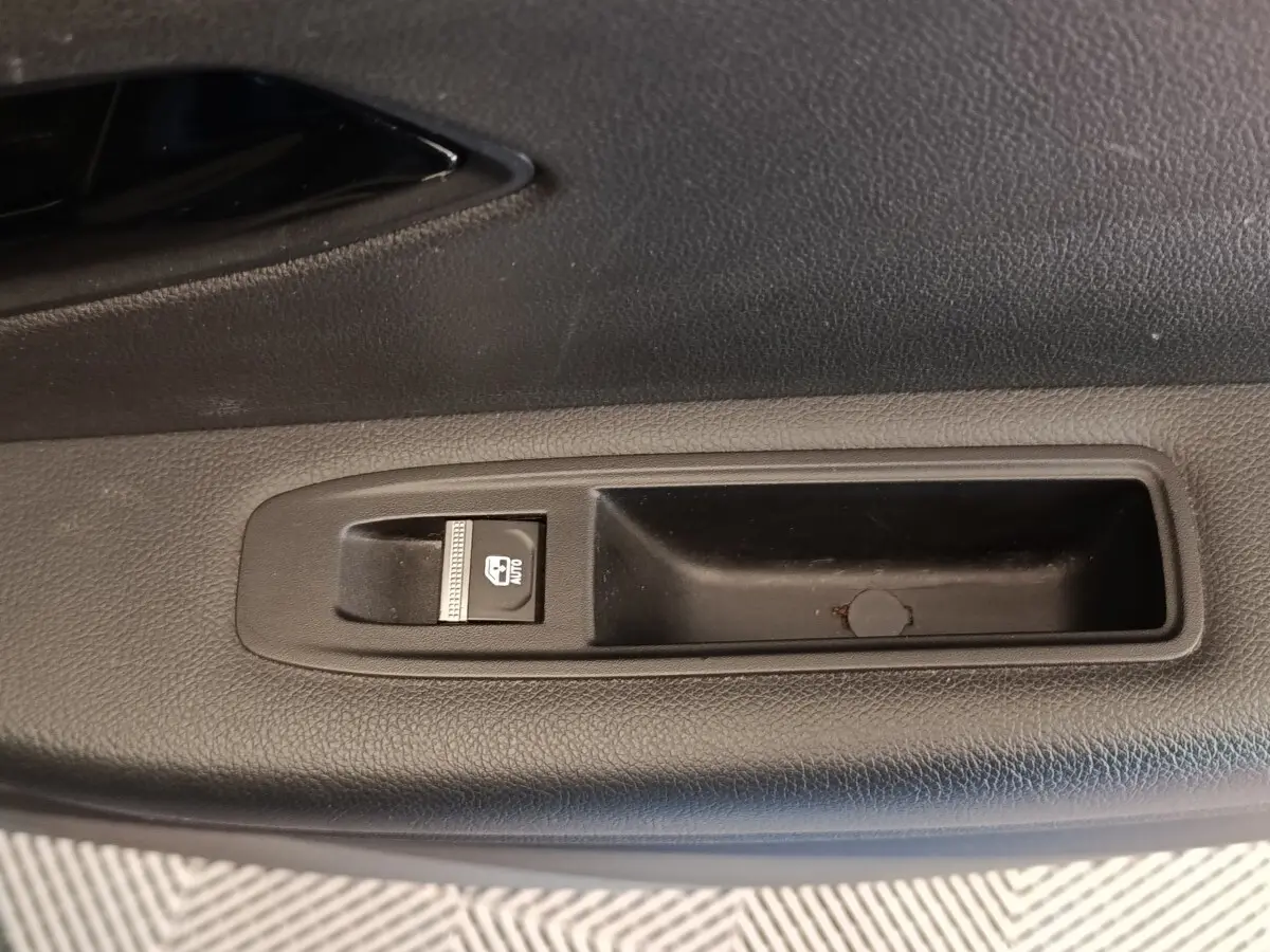 Gros plan sur le bouton de commande de la vitre électrique côté conducteur dans l'habitacle noir d'une Renault Mégane.