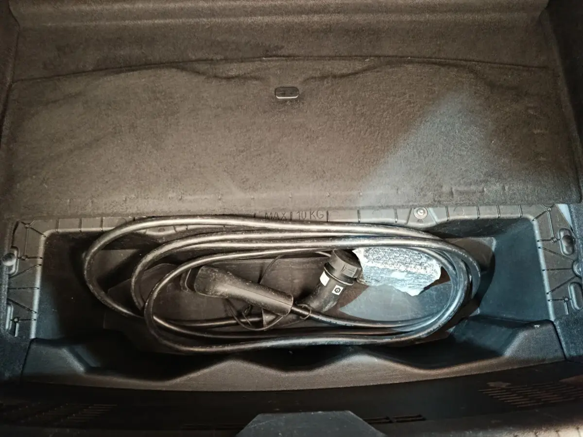 Vue plongeante sur le rangement sous siège arrière d'une Renault Mégane électrique avec câble de recharge noir enroulé.