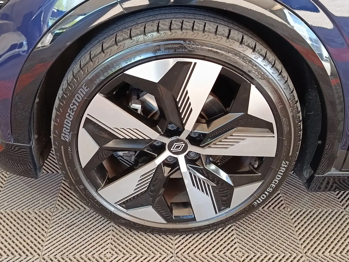 Gros plan sur la roue avant droite de la Renault Mégane Techno EV60 bleu, jante alliage design noir et argent.