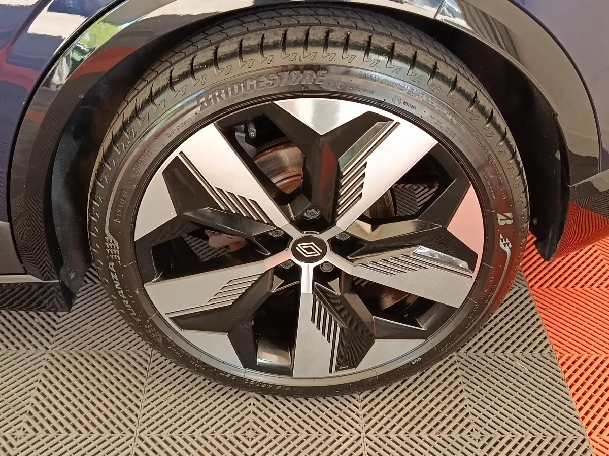 Gros plan sur la roue avant gauche de la Renault Megane Techno EV60 bleu, jante alliage noire et argentée au design géométrique.