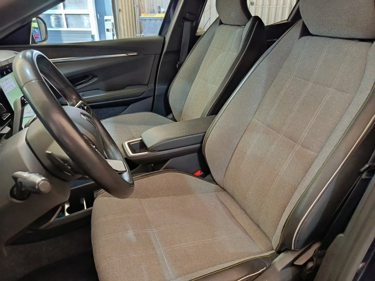 Vue intérieure côté conducteur de la Renault Megane Techno EV60 2023, sièges tissu gris clair avec surpiqûres contrastées.