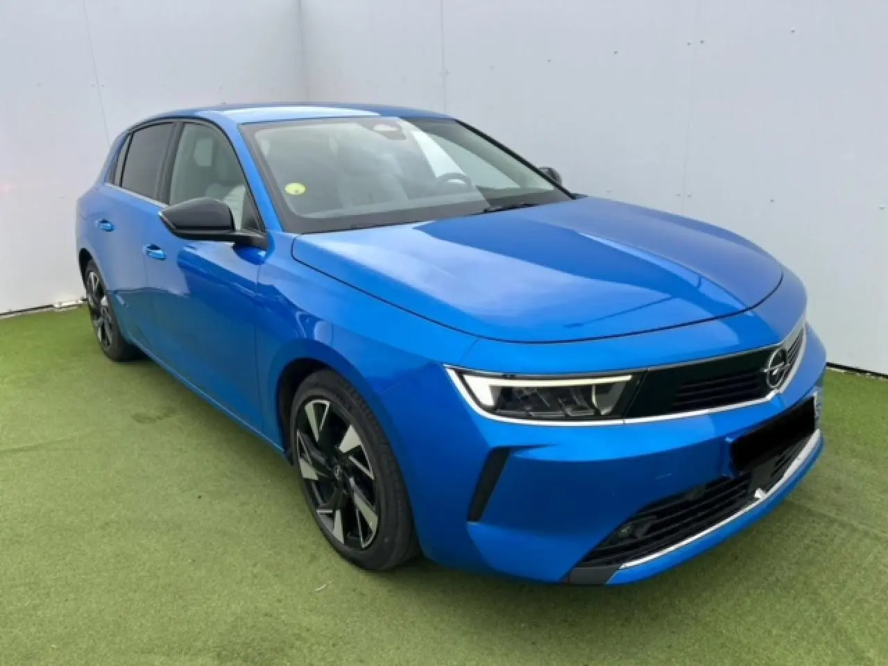 Opel Astra VI bleu clair vue 3/4 avant droit avec jantes alliage noires et calandre moderne noire.