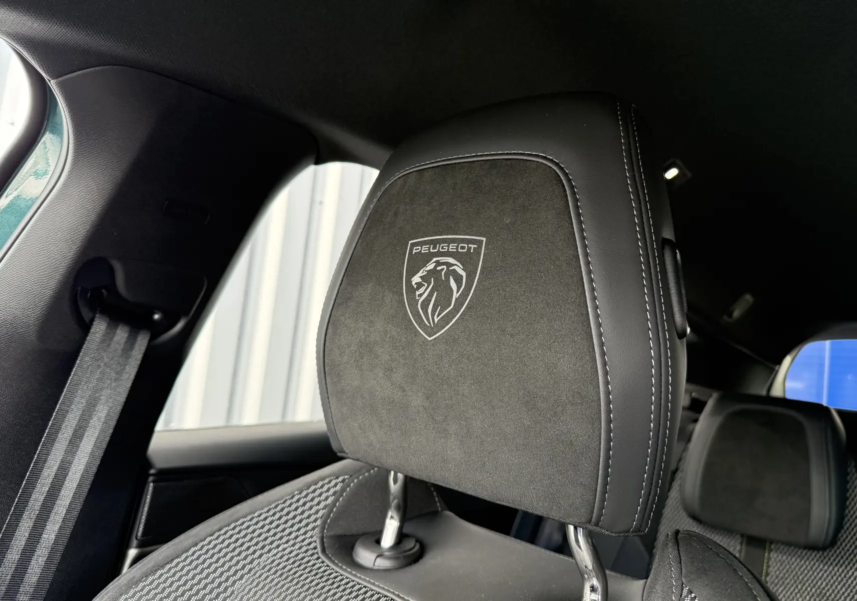 Gros plan sur l'appui-tête avant en cuir noir et alcantara avec logo Peugeot dans l'habitacle du 308 SW bleu Avartar.