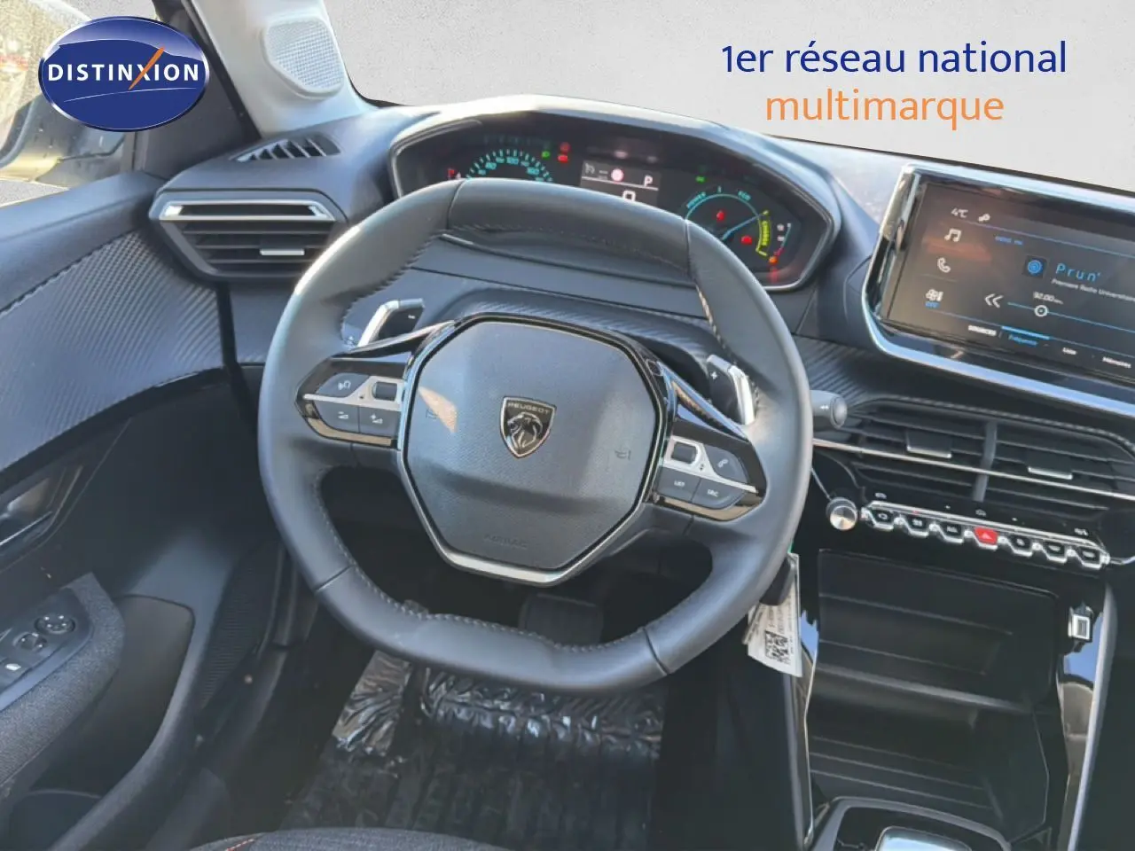 Vue intérieure centrée sur le volant cuir noir du Peugeot 208 hybride 2025 avec tableau de bord digital et écran tactile.