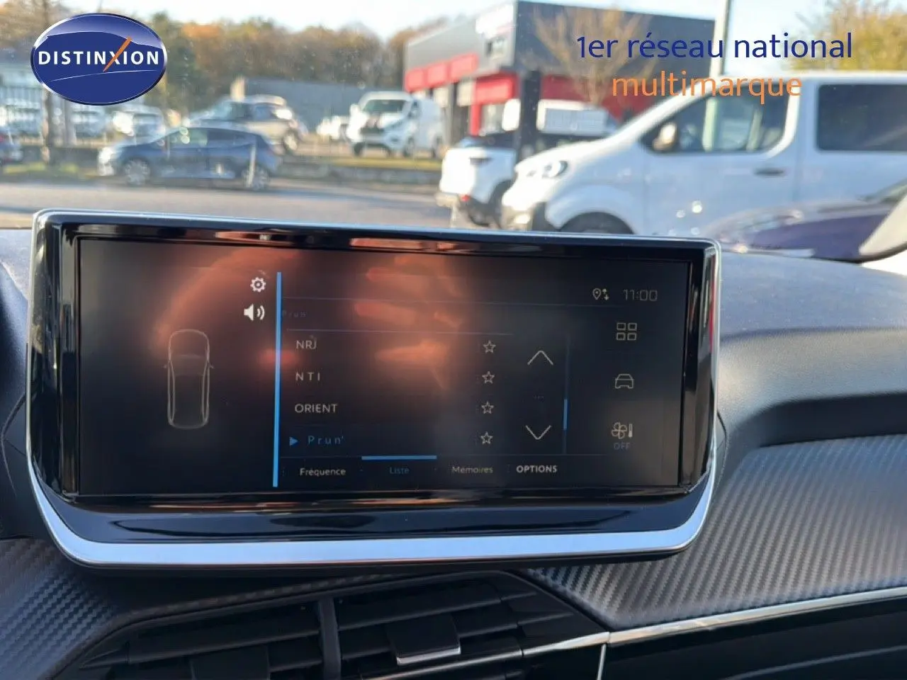 Écran tactile central du tableau de bord de la Peugeot 208 hybride 2025 avec finition gris artense métal visible à l'extérieur.