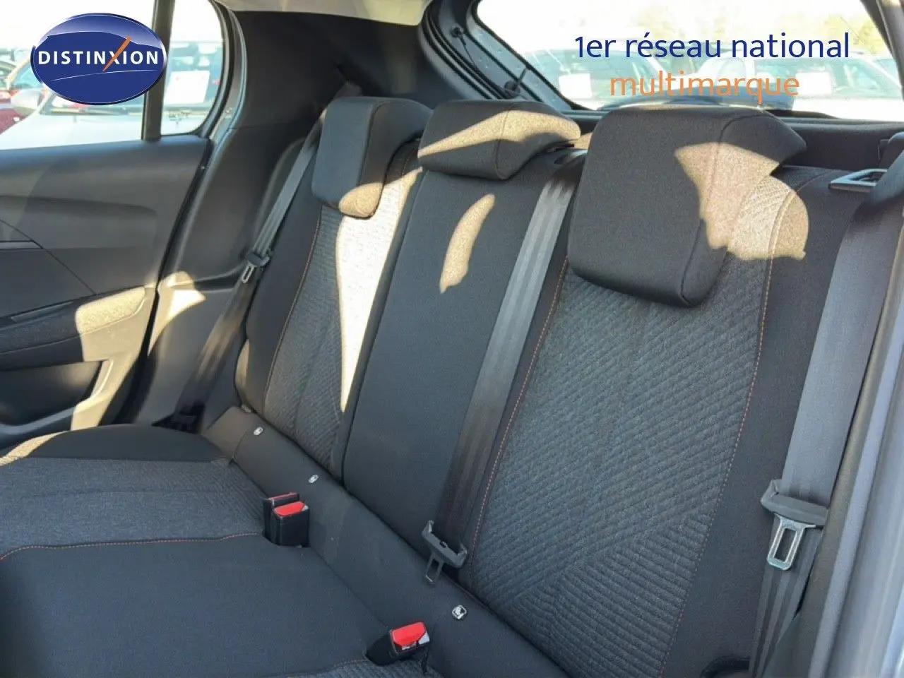 Vue intérieure sur les sièges arrière en tissu gris et noir de la Peugeot 208 hybride 2025, avec ceintures et appuie-têtes visibles.