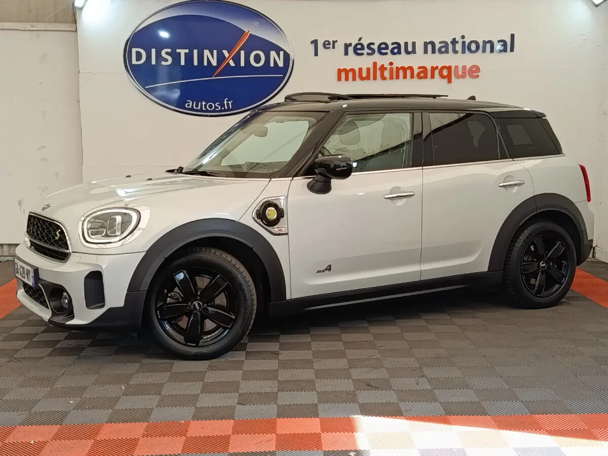 Vue latérale droite d'une MINI Countryman Cooper SE hybride blanche avec toit noir et jantes noires en intérieur showroom
