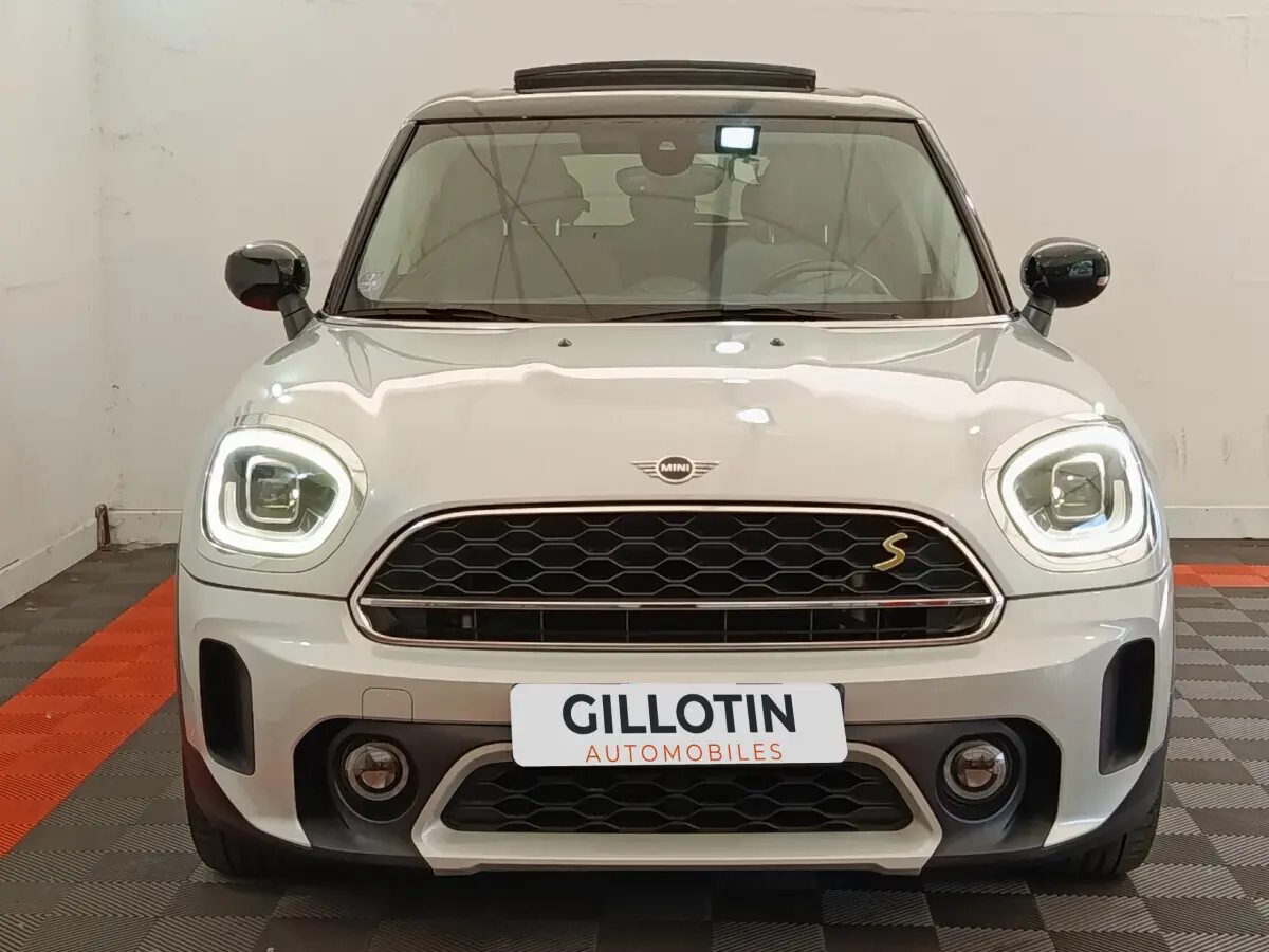 Vue frontale d'une MINI Countryman Cooper SE blanche avec phares LED allumés et calandre noire hexagonale.