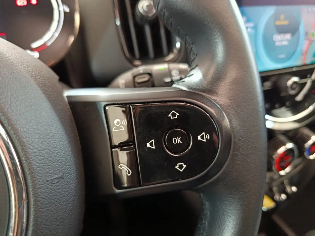 Gros plan sur les commandes vocales et téléphone du volant cuir noir d'une MINI Countryman blanche, tableau de bord en arrière-plan.