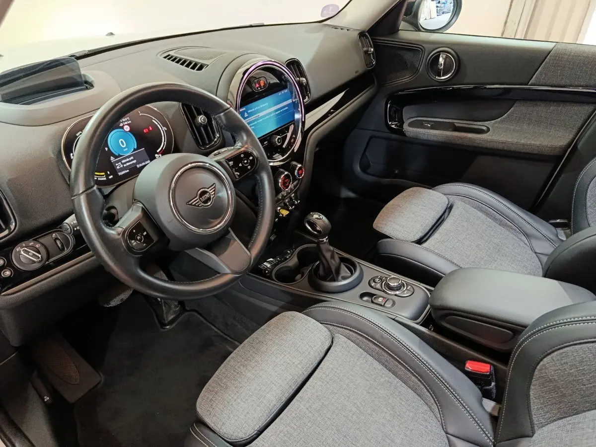 Intérieur avant droit du MINI Countryman Cooper SE, tableau de bord noir avec écran tactile circulaire et sièges tissu gris.