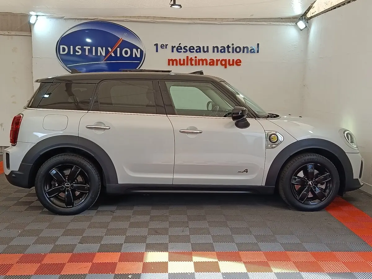Profil droit d'un MINI Countryman Cooper SE blanc avec toit noir et jantes noires dans un showroom intérieur.