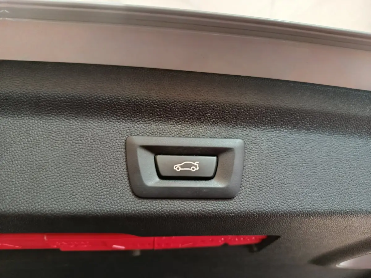 Gros plan sur le bouton d'ouverture électrique du coffre, intérieur noir texturé du hayon du MINI Countryman blanc.
