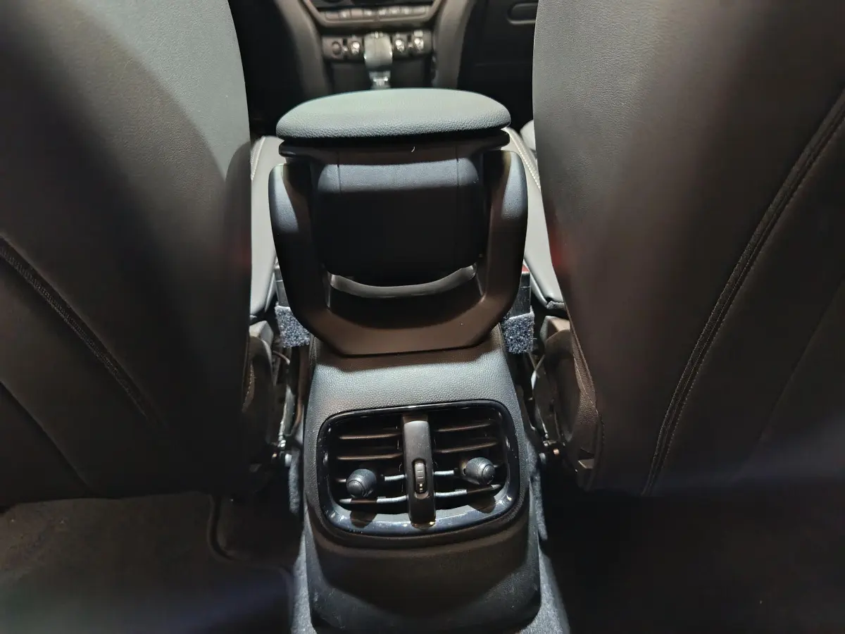 Détail des aérateurs arrière noirs entre les sièges avant en cuir foncé du MINI Countryman hybride blanc.
