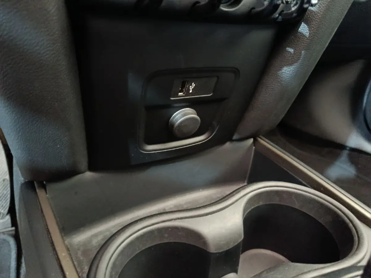 Prise USB et allume-cigare noirs en gros plan dans l’espace entre les sièges avant du MINI Countryman blanc 2021.