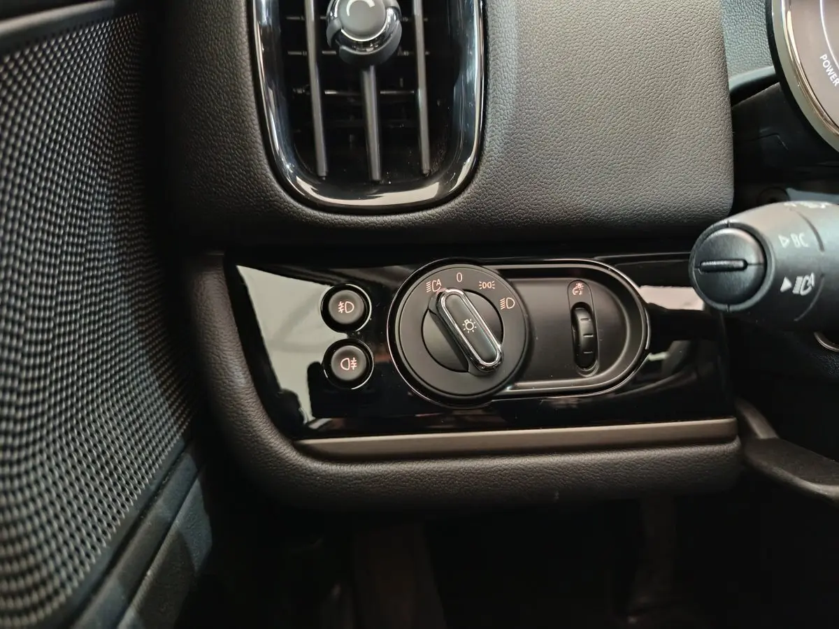 Gros plan sur la commande des phares noire brillante côté gauche du tableau de bord du MINI Countryman blanc 2021.