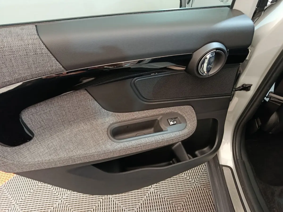 Gros plan sur la porte avant droite blanche du MINI Countryman Cooper SE avec habillage tissu gris et poignée chromée.